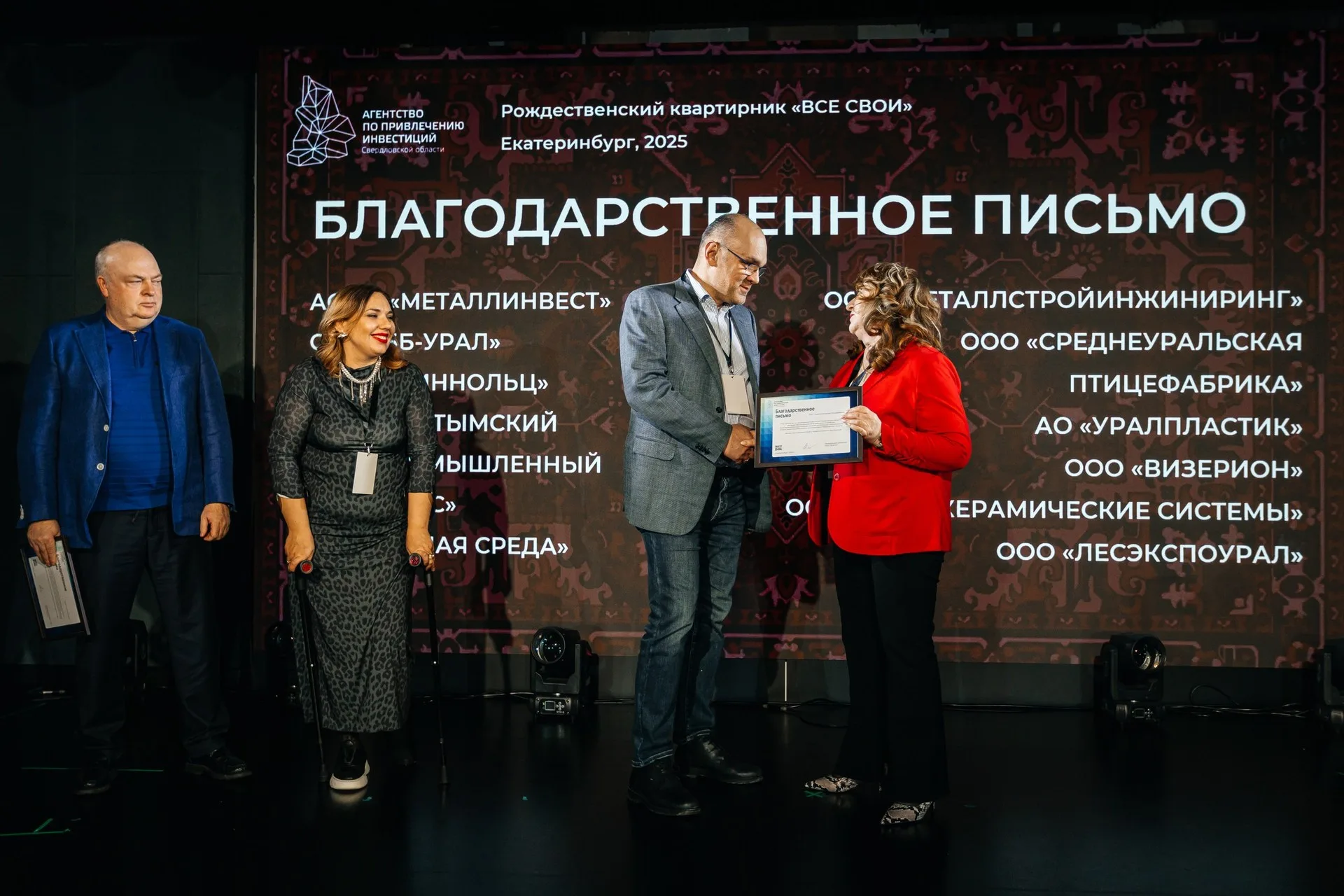 Две женщины позируют на фоне золотого текстильного шатра с длинной бахромой; вокруг — хвойные ветви и подсвеченные гирляндами деревья.