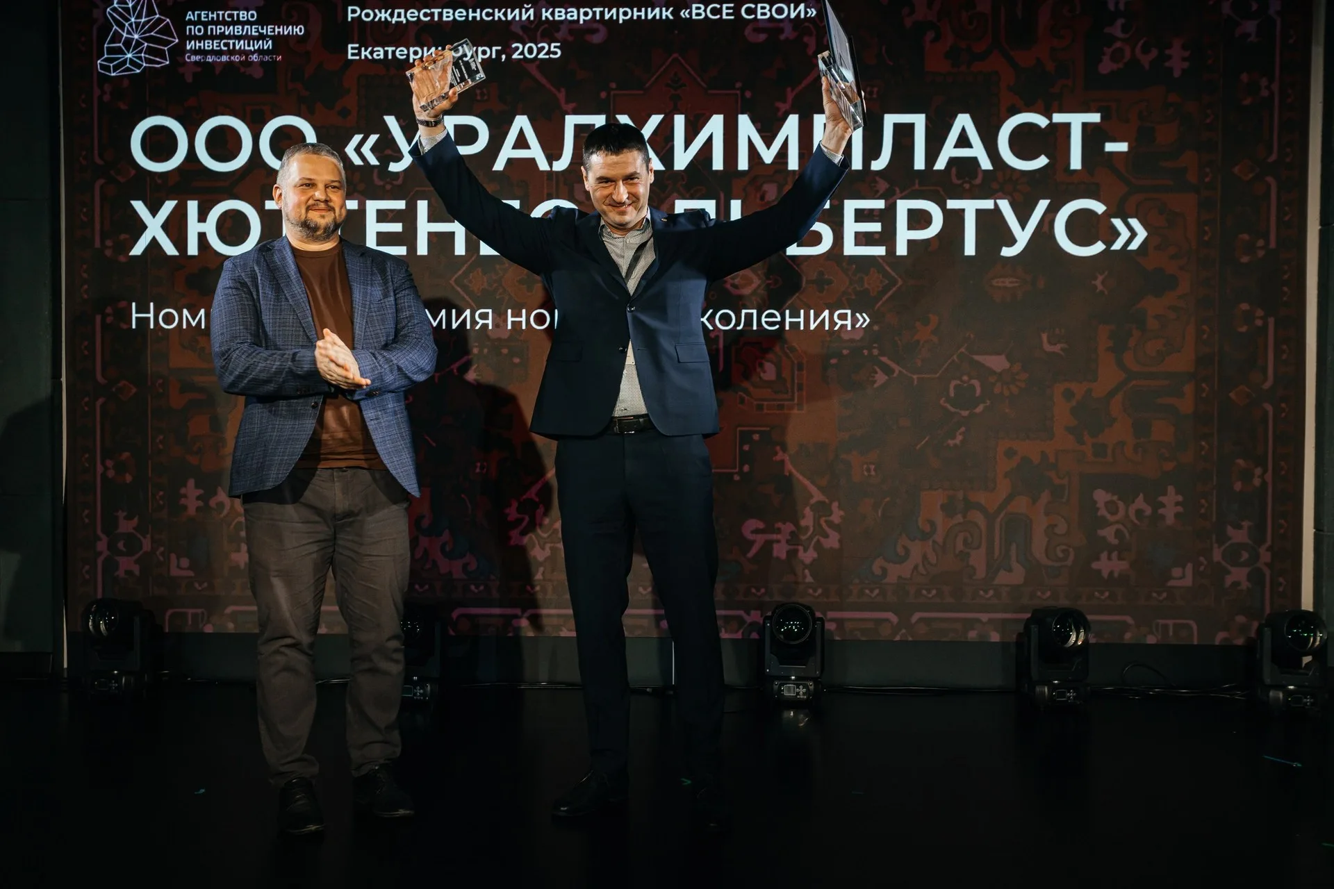 Две женщины позируют на фоне золотого текстильного шатра с длинной бахромой; вокруг — хвойные ветви и подсвеченные гирляндами деревья.