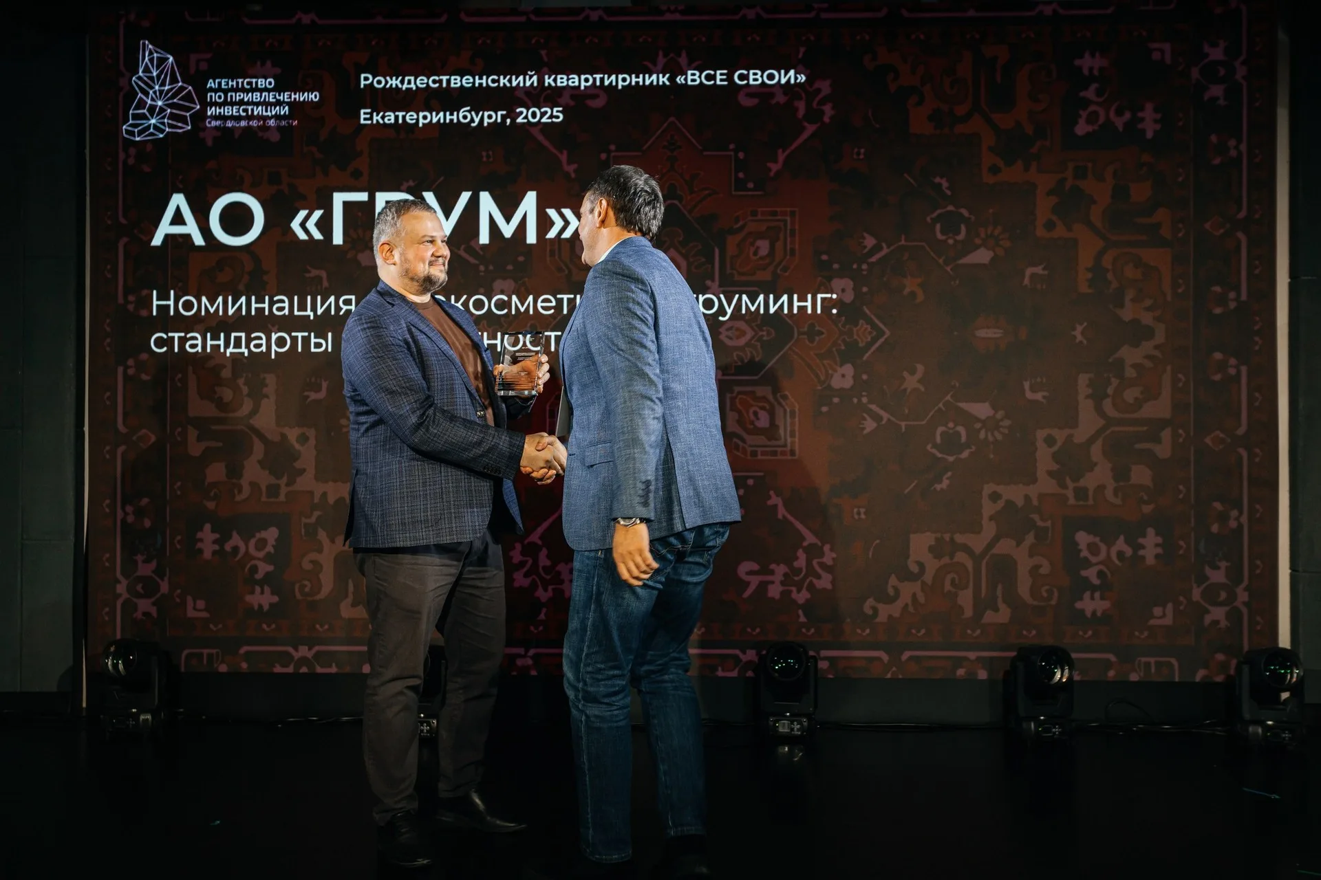 Две женщины позируют на фоне золотого текстильного шатра с длинной бахромой; вокруг — хвойные ветви и подсвеченные гирляндами деревья.