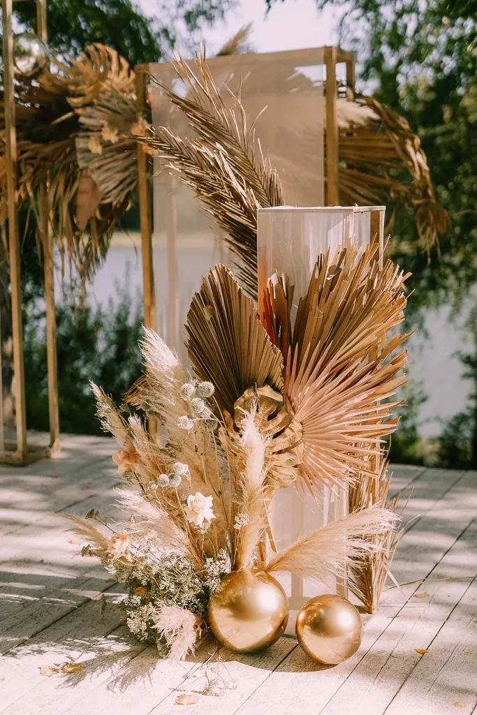 Руки в белых перчатках складывают пирамиду из бокалов с красным напитком на светлой узорчатой скатерти.