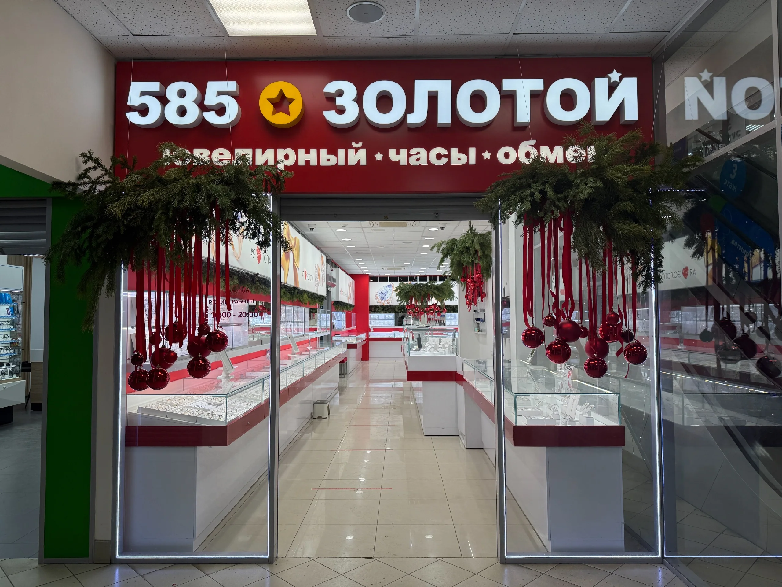 Под потолком магазина подвешена пышная еловая композиция с красными лентами и блестящими и матовыми шарами